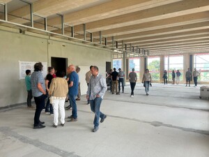 Das Foto zeigt eine Innenansicht des VOITH Bürogebäudes in der Rohbauphase. Es ist Richtfest und viele Gäste tümmeln sich auf dem Stockwerk. Man sieht eine Holzbalkendecke und eine Fensterfront.