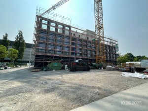 Das Foto zeigt eine Baustelle in Aktion. Es wird ein Hybridprojekt realisiert. Der Massivbaukern sowie eine fortgeschrittene Teilmontage der Stockwerke aus Holzelementen ist zu sehen.